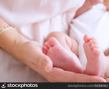 Mother hand holding cute tiny baby feet, doing massage for little newborn child, happy motherhood, protection and safety concept