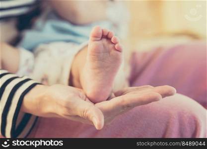 Mother hand holding feet baby child with careful.