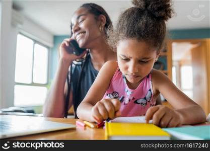 Mother helping and supporting her daughter with online school while talking on the phone at home. New normal lifestyle concept. Monoparental concept.
