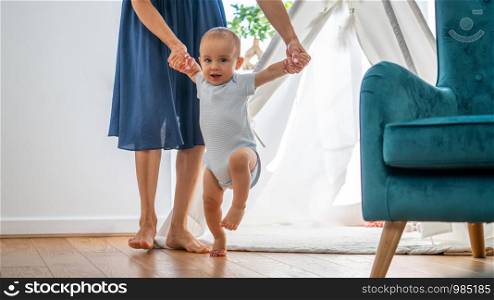 Mother Helping Baby Son To Take First Steps At Home