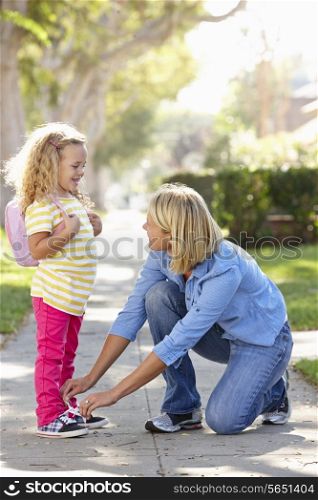Mother Helping Daughter Tie Shoe Laces On Walk To School