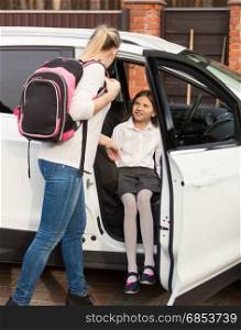 Mother helping daughter to get inside the car after school lessons