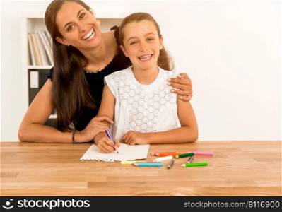 Mother helping her little daughter making drawings