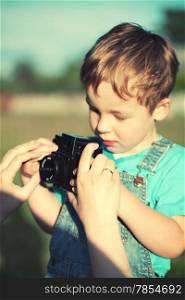 Mother helping her little son to take his first pictures outdoor. Focus on mothers hands. Instagram style color toned