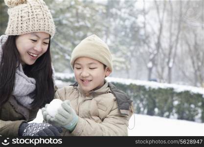 Mother helping son make snow ball