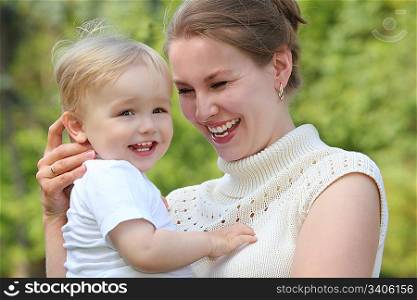 Mother hold baby on hands outdoor in summer and looks on him, focus on mother