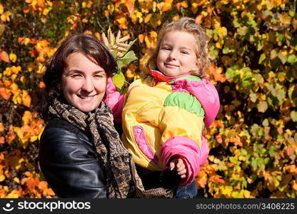 Mother hold daughter on hands on walk in autumnal park