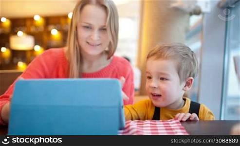 Mother holding a touchpad and watching her son playing with interest