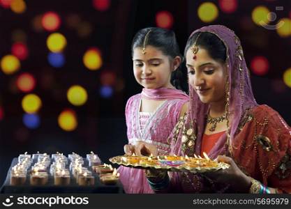 Mother holding a tray of diyas while her daughter looks on