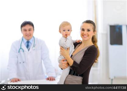 Mother holding adorable baby and doctor in background&#xA;