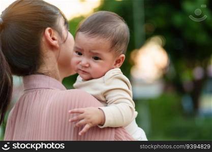 mother holding and comforting her crying infant baby outside in the park with sunlight