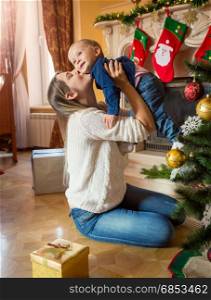 Mother holding and playing with her baby son on floor at Christmas tree