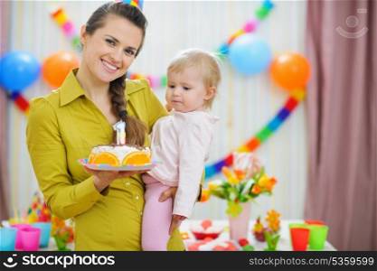 Mother holding baby and birthday party cake