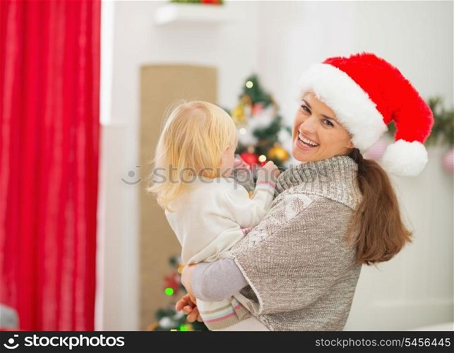 Mother holding baby in front of Christmas tree