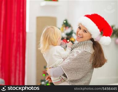 Mother holding baby in front of Christmas tree