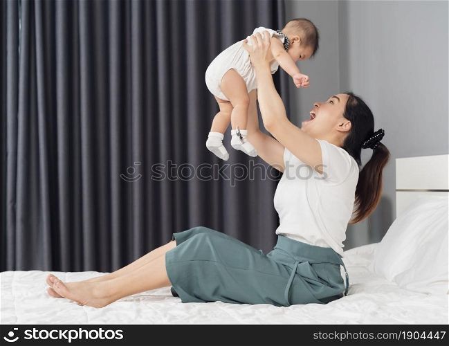 mother holding baby newborn in her arms lifting up on a bed at home