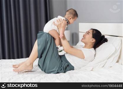 mother holding baby newborn in her arms lifting up on a bed at home