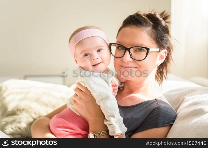 Mother holding beautiful baby girl in bright sunny room. Motherhood background. Mother holding beautiful happy baby girl in bright sunny room. Motherhood concept
