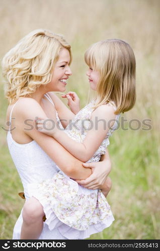 Mother holding daughter outdoors smiling