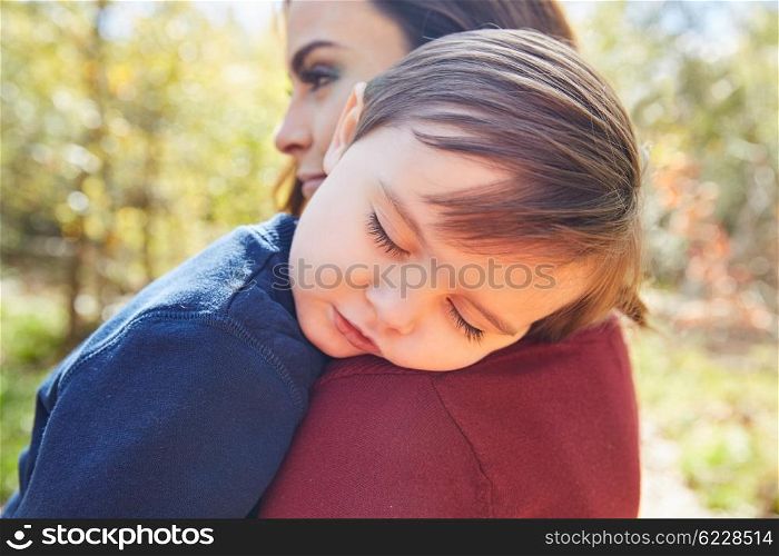 Mother holding kid boy sleeping in her shoulder at park