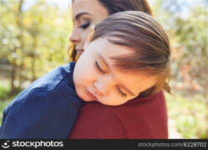 Mother holding kid boy sleeping in her shoulder at park