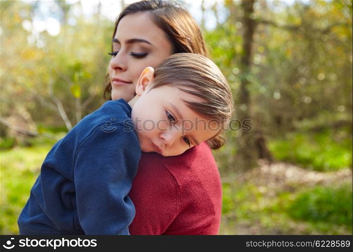 Mother holding kid boy tired in her shoulder at park