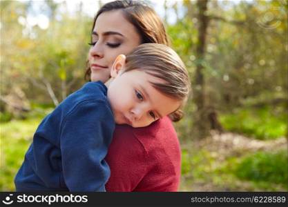 Mother holding kid boy tired in her shoulder at park