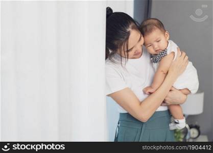 mother holding newborn baby in a tender embrace near window in the bedroom