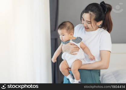 mother holding newborn baby in a tender embrace near window in the bedroom