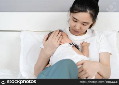 mother holding newborn baby sleeping in her arm on a bed