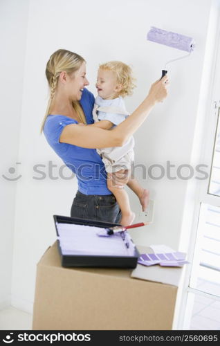 Mother holding son while painting room in new home smiling