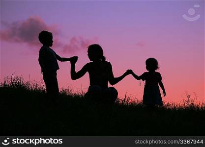 mother holds children for the hands on the sunset