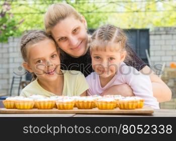 Mother hugging her daughters who cook delicious cupcakes