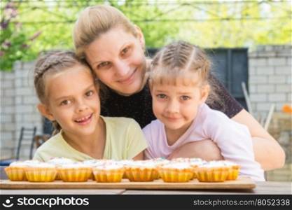 Mother hugging her daughters who cook delicious cupcakes