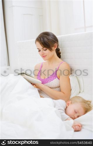 Mother in bedroom reading book while baby sleeping