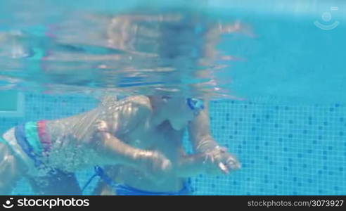 Mother is giving her son a swimming lesson in pool, she is holding him under water.