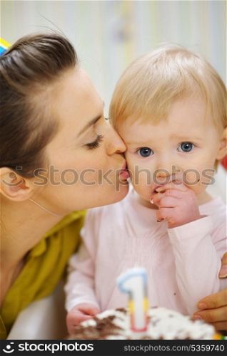 Mother kissing baby eating birthday cake