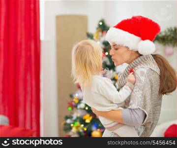Mother kissing baby in front of Christmas tree
