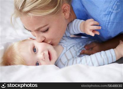 Mother Kissing Baby Son As They Lie In Bed Together