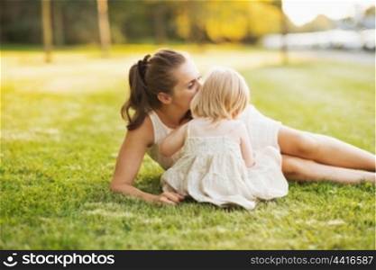 Mother kissing baby while sitting on meadow in park