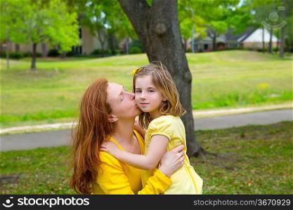 Mother kissing her blond daughter in green park outdoor dressed in yellow