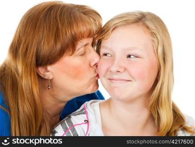 Mother kissing her pretty blond daughter who looks embarassed. White background.