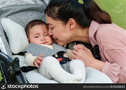 mother kissing with her infant baby in the stroller while resting in the park