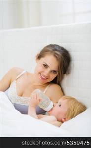 Mother laying near drinking water baby in bed