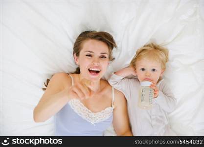 Mother laying with baby in bed and pointing in camera. Upper view