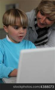mother learning her little boy how to write on a laptop