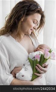 mother looking her baby with holding pink tulip flowers home