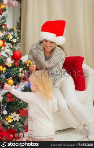 Mother looking on baby decorating Christmas tree