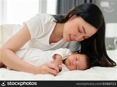 mother lying down and looking her newborn baby on a bed. 