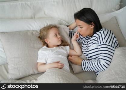 Mother lying in comfortable bed with small foster girl in bedroom together. Mom wake up little daughter after sleeping in the morning at home. Healthy sleep in children, childcare.. Mother lying in comfortable bed with foster daughter after sleeping. Healthy sleep in children